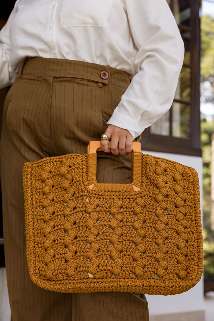Circulo Fio Náutico Poly 5 mm – Polyester Cord Yarn ( 178 m / 500 g) - A person wearing a white button-up shirt and brown pinstriped trousers holds a large, textured mustard-yellow crocheted tote bag with tan handles.