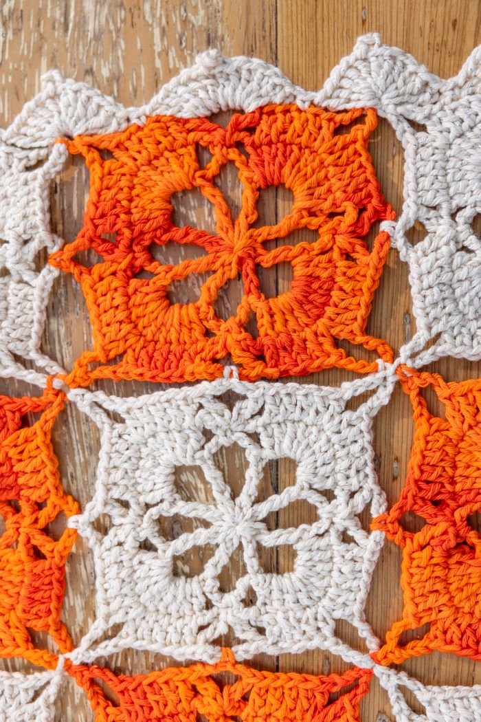 Círculo Natural Cotton Multicolor 4/6 – Cotton Yarn (226 m / 200 g) – A close-up of a crocheted textile featuring alternating orange and off-white granny square panels on a light wood background.