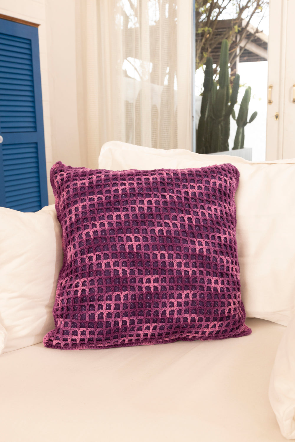 Círculo Natural Cotton Multicolor 4/6 – Cotton Yarn (226 m / 200 g) – A square throw pillow with a textured, woven geometric arch pattern in shades of purple and pink, resting on a white sofa in a brightly lit room.