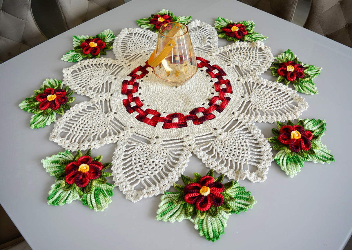 Circulo Barroco Natural Brilho  - Natural Cotton Yarn Gold/Silver, 657m / 433m, 400g - A crocheted holiday table runner or doily set on a gray table, featuring white lace petals with red and green poinsettia flowers and a central red-and-black pattern, with a small glass bottle placed on top.