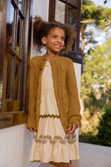 Circulo InLove  - 100% Brazilian Cotton Yarn  (125m/100g) - A young girl with curly hair stands outdoors wearing a cream-colored dress with a textured mustard-brown cardigan.