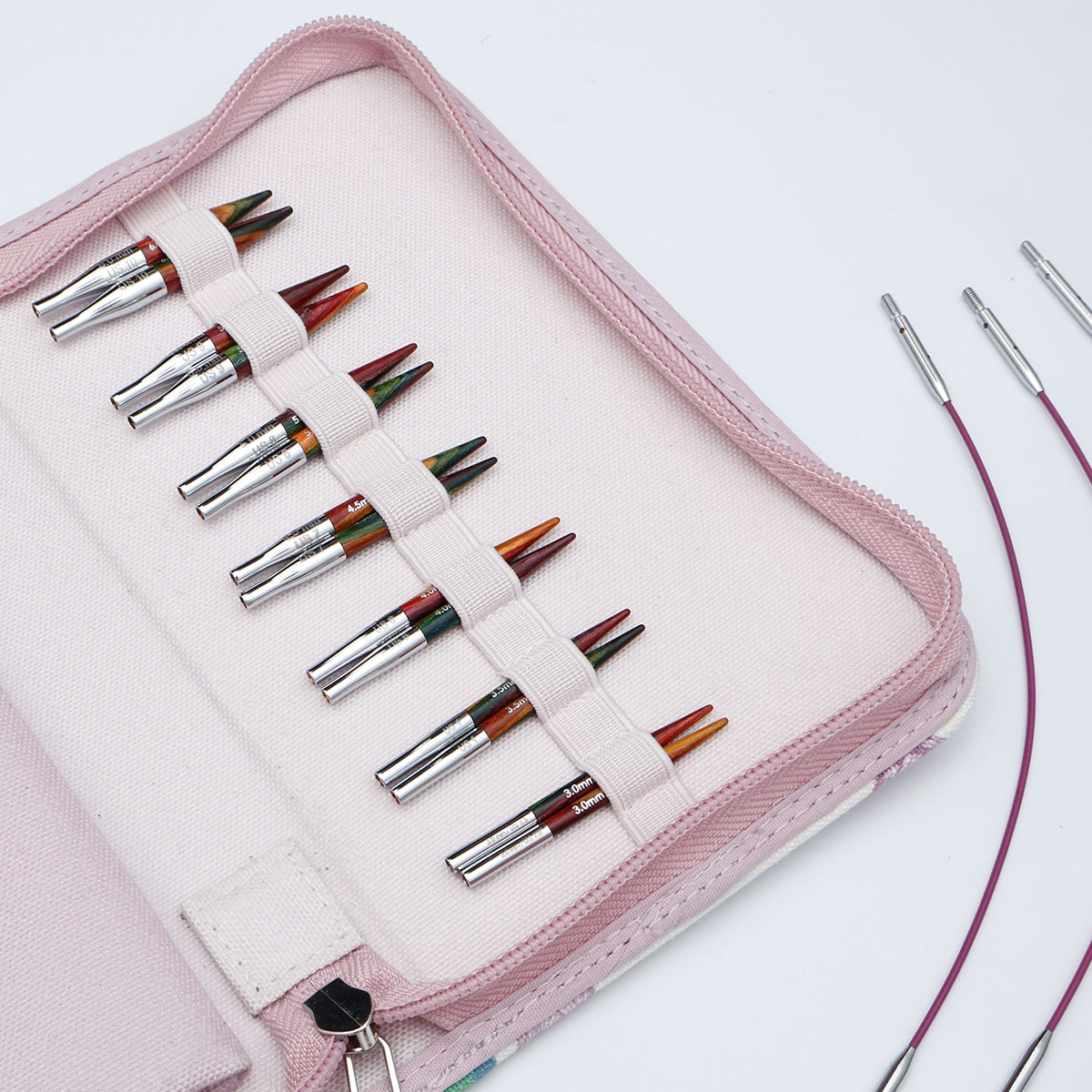 KnitPro Symfonie 2 Mini interchangeable needle set, 5 cm - A pink zippered carrying case holding multiple knitting needles arranged in elastic loops. The needles have silver metal shafts and tips with multicolored yarn wrapped around them.